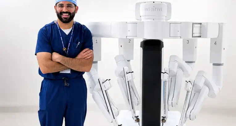 General surgeon Dr. Shyamal Pansuriya smiling alongside the new da Vinci 5 robotic surgical system at Artesia General Hospital.
